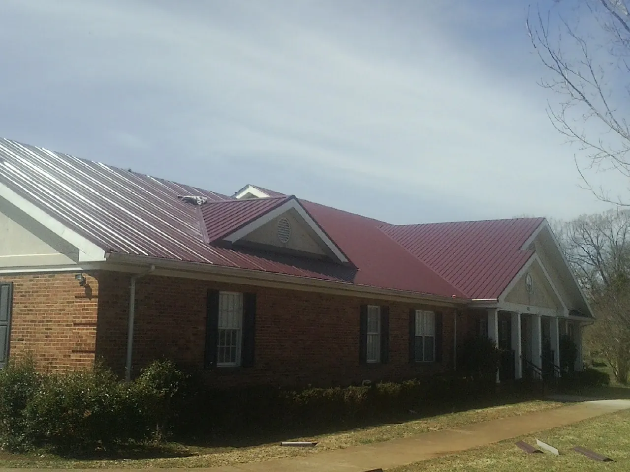 Red metal roof with gabled entries on a long brick building, from a Hail Damage Roof Repair job in Paramus