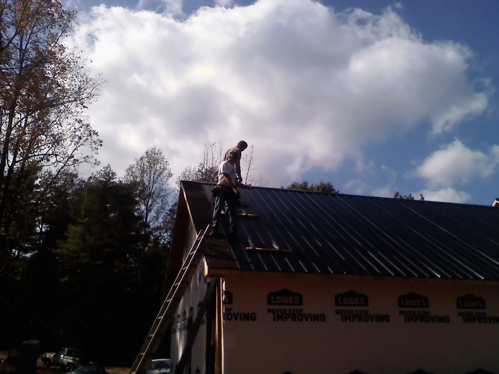 Roofer fastening dark metal panels high against a cloudy sky, from a Roof Inspection job in Paramus