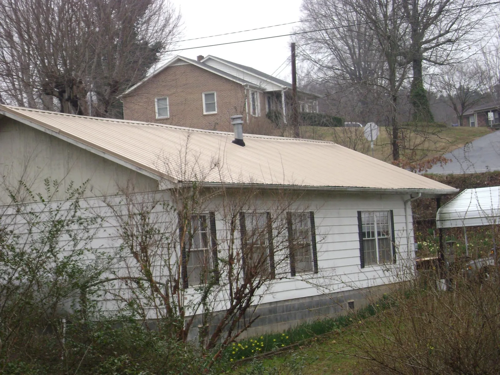 Tan metal roof on a white sided house set into a hillside — Commercial Roofing by Roofing Brothers in Paramus